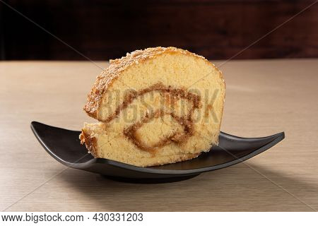 Rocambole, Slice Of Roacambole Stuffed With Sweet Bed On A Black Plate On A Table. Dark Background, 