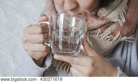 A Young Woman Has A Cold And Drinks Medicine. The Girl Her Throat With A Scarf And Drank Hot Water. 