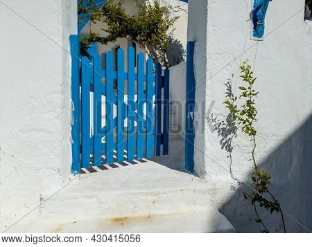 Blue wooden opened fence gate of whitewashed traditional building. Koufonisia island, Cyclades architecture, destination Greece. Welcome door, stairs, plants, summer tourism explore vacation sunny day