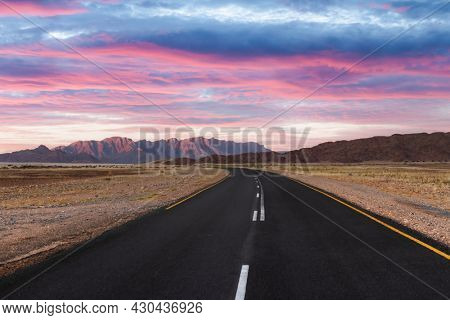 Asphalt road through desert savanna in of Namib at Namib-Naukluft National Park in Namibia, Africa. Highway and sunset sky