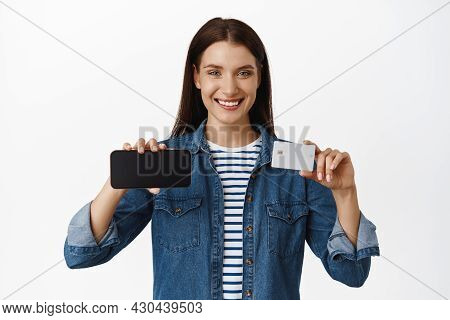 Image Of Smiling Attractive Woman Showing Horizontal Screen Smartphone, Credit Card In Hand, Looking