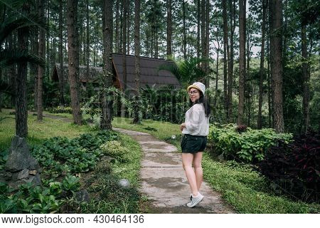 Winter Travel Relax Vacation,portrait Asian Female Tourist In White Dress With Hat Stands In Pinewoo