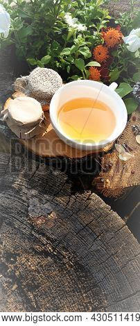 A Cup Of Tea With A Saucer On A Wooden Stand With A Jar Of Honey And Flowers