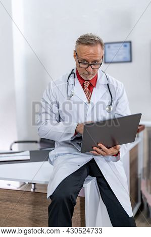 Portrait Of Male Doctor Checking Documents In Clinic On Laptop. Healthcare Workers In The Coronaviru