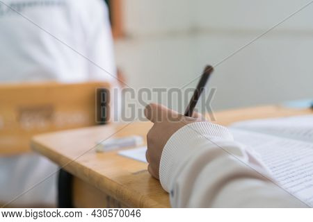 Writing On Exam Test In Classroom. Asian Young Student Holding Pencil Taking Exams On Answer Sheet E