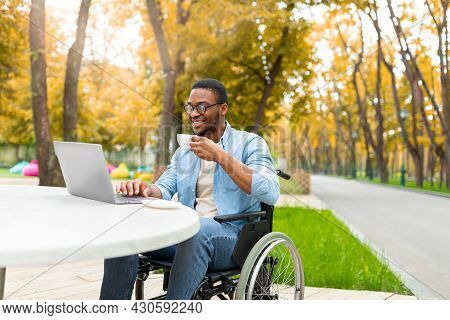Remote Job For Impaired People. Cheerful Black Guy In Wheelchair Working Online, Using Laptop At Out