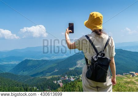The Traveler In A Hat, Resting In Nature. A Tourist Girl Photographs A Panorama Of The Mountains By 
