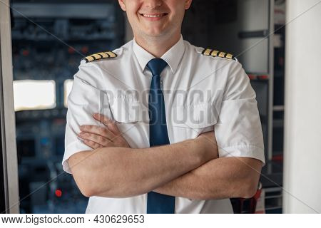 Cropped Portrait Of Male Pilot In Uniform Keeping Arms Crossed And Smiling While Posing, Standing In