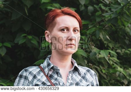 Simple Portrait Of A Red-haired Young Woman With Short Hair. Woman In A Checkered Shirt Against The 
