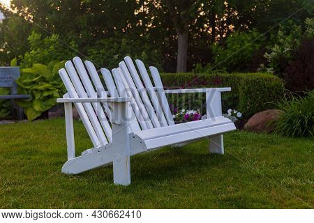 White Adirondack Double Chair Overlooking In A Garden Setting.