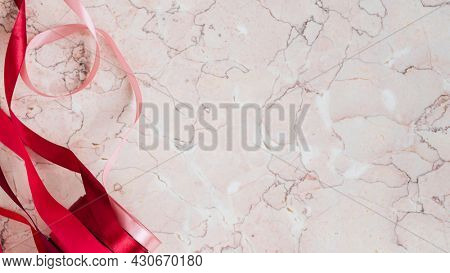 Rolls of red ribbon on a pink marble background
