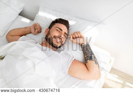 Happy Wellslept Guy Waking Up In Morning, Stretching While Lying In Comfortable Bed And Smiling, Hig
