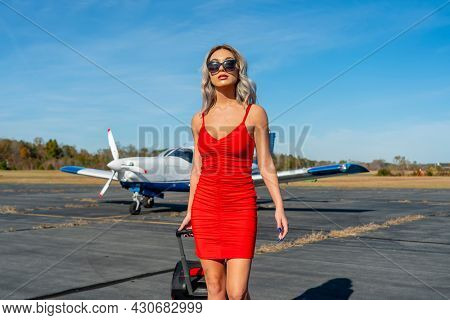 A gorgeous young blonde model poses outdoors with a single engine aircraft at a local airport