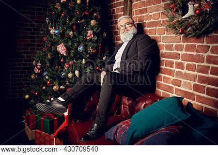 Merry Christmas and Happy New Year! Portrait of a handsome mature man with gray beard and gray hair celebrating Christmas at home. Loft interior with New Year decorations.
