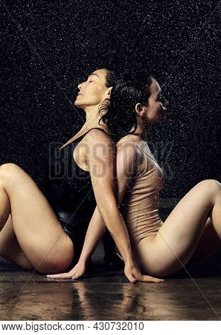 Two Beautiful Women Of Caucasian Appearance With Black Hair Sit Back To Back In Drops Of Water On A 