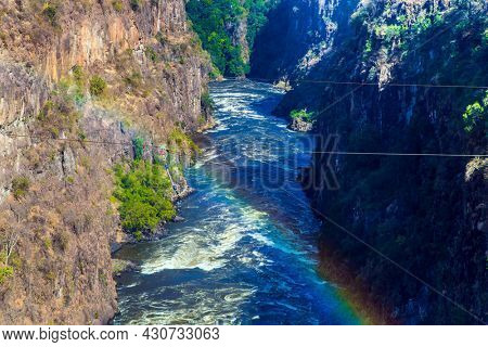 Gorgeous rainbow. Ropes for canopy stretched over a canyon with a raging  african Zambezi River. The waterfall Victoria Falls on the Zambezi River. Concept of extreme and photo tourism