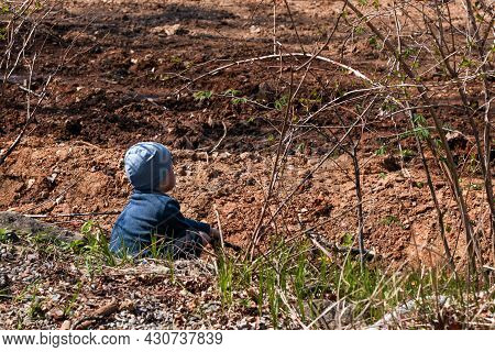 A Boy Sits On The Ground In A Spring Park. High Quality Photo