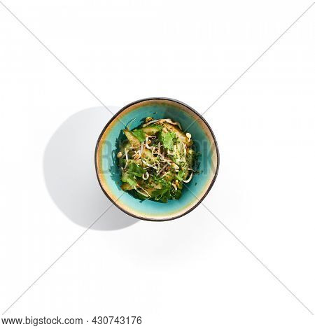 Chinese smashed cucumber with greens and sesame oil. Healthy vegetarian green salad with cracked cucumber and fresh green leaf. Healthy salad recipes concept. Salad bowl isolated on white background