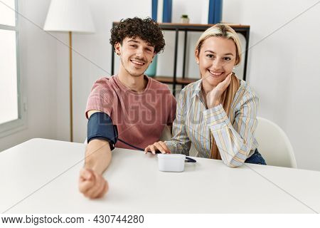 Young couple smiling happy measuring blood pressure using tensiometer at home.