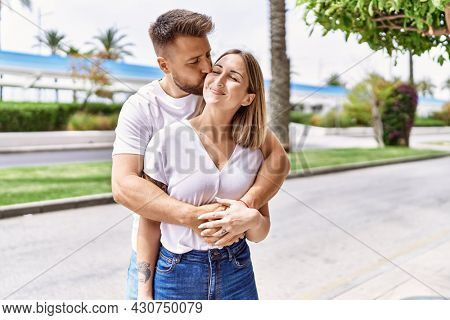 Young caucasian couple of boyfriend and girlfriend having fun outdoors on a un sunny day kissing and hugging in love