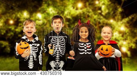 holiday and childhood concept - happy children in halloween costumes trick-or-treating over lights at night garden background