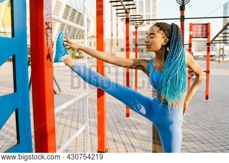 Young african fitness woman stetching her leg while standing at the sportsground