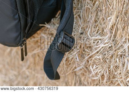 A Close-up Of The Black Strap Of The Backpack Against The Yellow Hay. Black Plastic Buckle That Adju