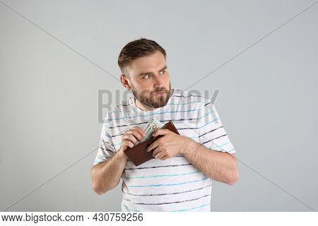 Greedy Young Man Hiding Wallet With Money On Light Grey Background