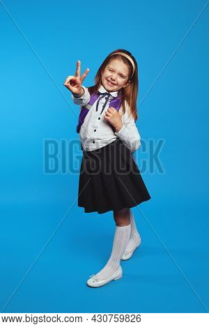 Back To School. Cute Young Schoolgirl Wearing Uniform And Backpack, Smiling While Showing Peace Gest