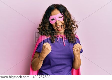 Middle age hispanic woman wearing super hero costume celebrating surprised and amazed for success with arms raised and eyes closed 
