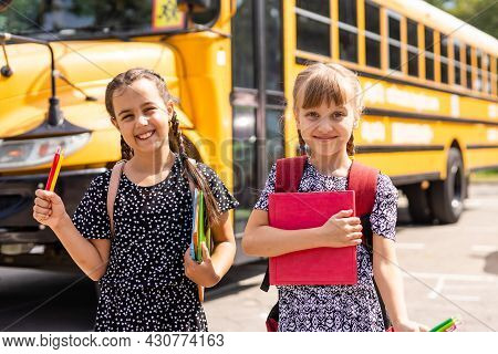 Cheerful Little Girls Next To School Bus. Backback. Back To School Concept.