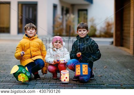 Little Toddler Girl And Two Kids Boys Holding Selfmade Lanterns With Candle For St. Martin Processio