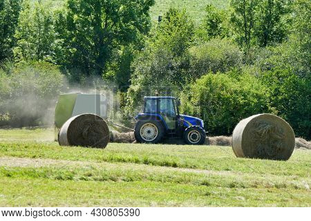 Tractor Pulling A Baler Over Lines Of Dry Cut Hay To Make Hay Bales For Animal Fodder