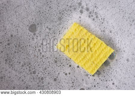 Cleaning Sanitation Concept. A yellow sponge floating in a sink full of soap suds and bubbles.