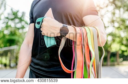 Strong man guy holding set of colorful elastic rubber bands at the stadium outdoors. Athlete male person during workout with additional sport equipmant