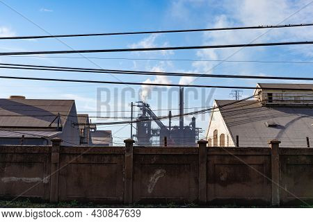 Steel Mill Blast Furnaces Behind A Tall Wall, Smokestacks And Smoke Into Blue Skies, Horizontal Aspe