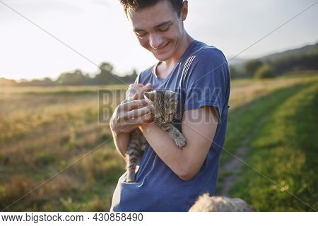Young Guy Found And Picked Up Little Stripped Kitten During Walking In The Field And Going To Home I