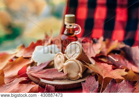 Maple syrup taffy cones dessert with traditional bottle and plaid cloth table - red leaves on table. Quebec local food.