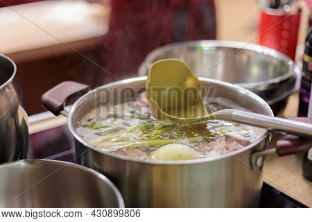 A Metal Saucepan Filled With Boiling Vegetable And Meat Broth. There Is A Scoop In The Broth. Close-