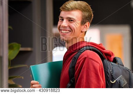 Rear View Of Beautiful Boy Walking Down A University Hallway, Looking Back And Smiling. The Student 