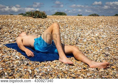 A 18 Year Old Caucasian Shirtless Teenage Boy Sunbathing On A Stoney Beach