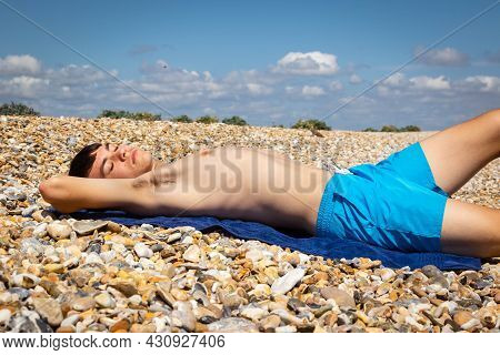 A 18 Year Old Caucasian Shirtless Teenage Boy Sunbathing On A Stoney Beach