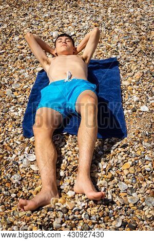 A 18 Year Old Caucasian Shirtless Teenage Boy Sunbathing On A Stoney Beach