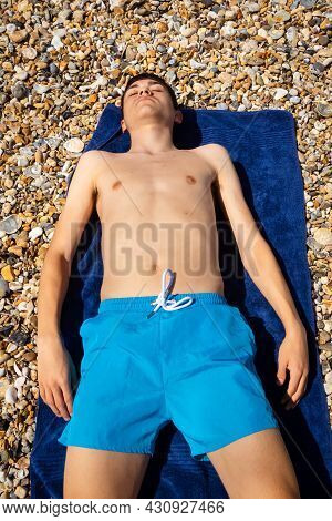 A 18 Year Old Caucasian Shirtless Teenage Boy Sunbathing On A Stoney Beach