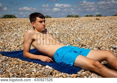 A 18 Year Old Caucasian Shirtless Teenage Boy Sunbathing On A Stoney Beach