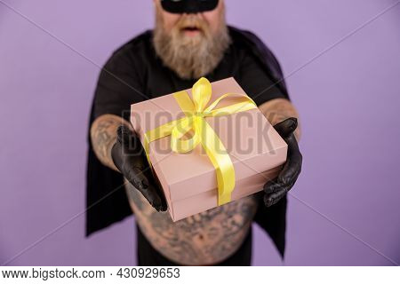 Man With Overweight In Carnval Costume On Purple Background, Focus On Hands With Gift Box