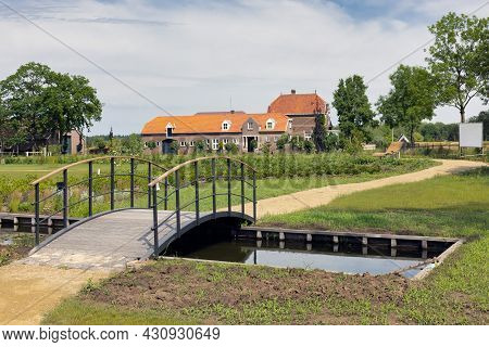 Dutch Public Park With Small Canal And Wooden Bridge Near Old Farmhouse