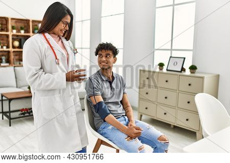 Young latin doctor woman smiling happy measuring pulse using tensiometer at the clinic.