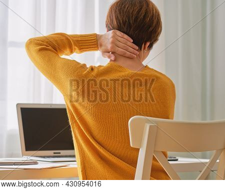 Back View Of Anonymous Female Sitting At Desk And Feeling Pain In Neck. Disadvantages Of Remote Work