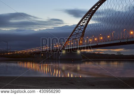 The Bugrinsky Highway Bridge Across The Ob River Stretches To The Horizon. Street Lights. Reflection